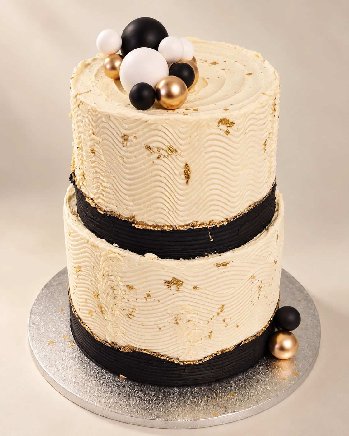 Two-tier ivory wedding cake with black bands, gold leaf and black, white and gold spheres